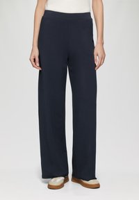 Marineblauwe wijde broek van een zachte stof met een elastische tailleband, voorzien van zijzakken en een gladde, onbewerkte afwerking.