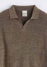 Pull-over en tricot marron avec un col court et un tissu texturé. Le design présente un motif chiné subtil et une étiquette.
