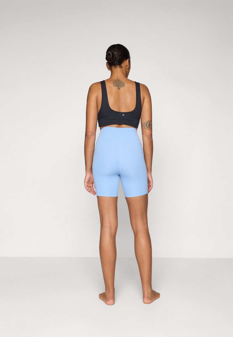 Schwarzes Sport-Crop-Top und hellblaue hochgeschnittene Shorts. Weicher Stoff, taillierter Schnitt, minimale Nähte und keine sichtbaren Logos oder Muster.