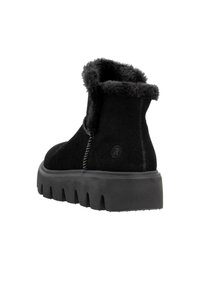 Botines de ante negros con un suave cuello forrado de piel. Suela negra gruesa y texturizada con un patrón en zigzag. Detalle de costura simple visible.