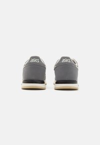 Gray athletic shoes with a suede upper, reflective accents, and a beige sole. The ASICS logo is displayed on the heel.
