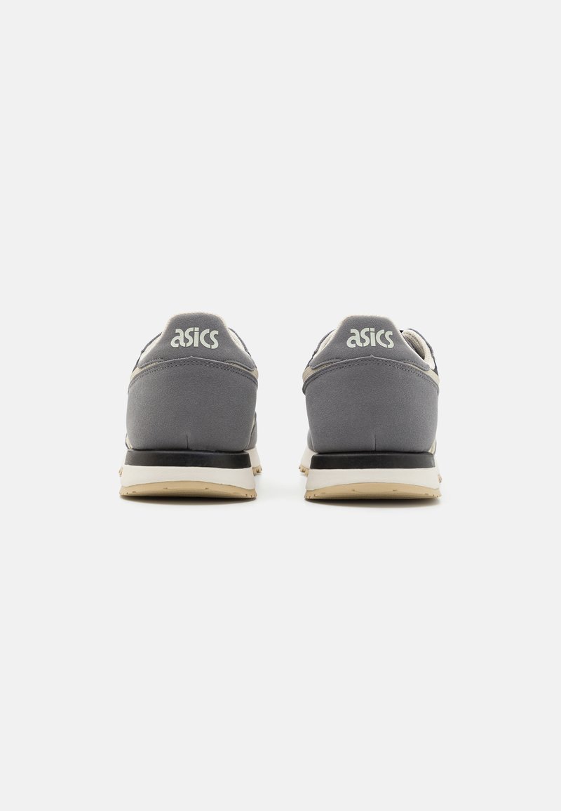 Baskets de sport grises avec une tige en daim, des accents réfléchissants et une semelle beige. Le logo ASICS est affiché sur le talon.