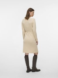 Beige neulemekko, jossa on vyötäröllä solmittava vyö, pitkät hihat ja suora leikkaus. Yhdistetty polven korkeisiin ruskeisiin nahkasaappaisiin. Sileä pinta.