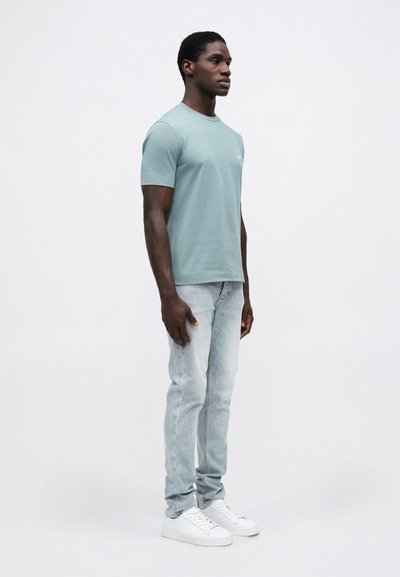 Svijetloplavi kratki rukav s okruglim dekolteom od pamuka, u kombinaciji sa svijetloplavim trapericama. Model nosi bijele tenisice. Minimalistički dizajn, bez vidljivih uzoraka ili logotipa.