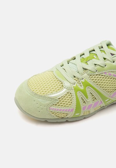 Basket vert clair avec tissu en mesh, bout en suède, lacets vert pâle et accents rayés violets sur le côté. Seule la partie avant est visible.
