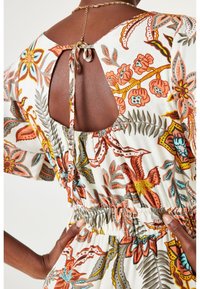 Frau in einem Blumenkleid mit offenem Rücken, das am Hals gebunden ist, mit elastischem Bund und kurzen Puffärmeln.