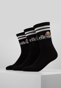 Calze di cotone nere con righe bianche in alto, caratterizzate da un logo che combina un triangolo e del testo. Tre paia esposti insieme.