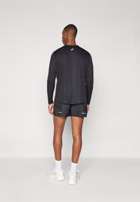 T-shirt de sport noir à manches longues et short noir avec des accents réfléchissants, associés à des chaussettes blanches et des baskets de couleur claire.