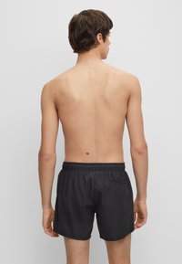 Pantaloni da nuoto neri con cintura elastica, frontale piatto e una piccola tasca laterale. Tessuto morbido e lunghezza sopra il ginocchio.
