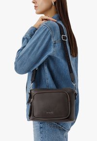 Mørkebrun læder crossbody taske med en tekstureret overflade, med en forlomma og justerbar rem med logo detalje.