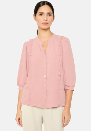 Light pink blouse with ruffled details along the placket, buttoned front, and three-quarter sleeves, made from a lightweight fabric.