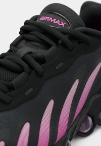 Black sneaker with mesh upper, pink accents, and rubber sole. Features rounded heel and prominent lacing system. "AIR MAX" logo at the tongue.