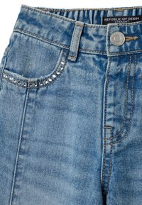 Jean en denim bleu avec une coupe droite, ornés d'une petite rangée décorative de strass le long du bord de la poche et d'un surfilage contrastant.