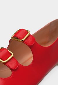 Κόκκινο δερμάτινο παπούτσι με διπλές χρυσές πόρπες και στρογγυλεμένες εγκοπές, που αποκαλύπτουν το ταμπά εσωτερικό φόδρα.