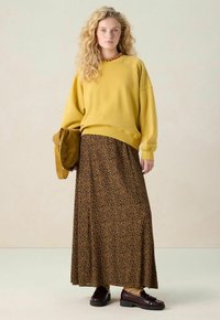 Geel oversized sweatshirt, maxi-jurk met bruin luipaardmotief en bordeauxrode schoenen. Accessoires zijn een bruine schoudertas en een houten ketting.