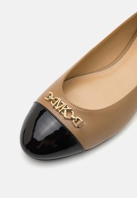 Ballerine con tomaia in pelle beige e punta in vernice nera. Presentano una catena dorata e un dettaglio con logo "MK" sulla parte anteriore.