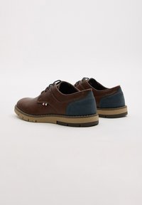 Zapatos de cuero marrón con un acento azul, punta redonda, diseño con cordones y suela de goma. Presentan detalles de costura y una franja de logo en el costado.