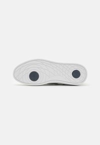 Weißer Sneaker-Außensohle mit geometrischem Profil und zwei runden schwarzen Akzenten. Glatte Textur mit flexiblem Design für besseren Halt.