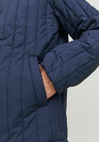 Giacca trapuntata blu marina con cuciture orizzontali, tasca laterale e vestibilità comoda. Realizzata in tessuto liscio e resistente all'acqua.