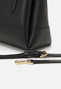 Czarna skórzana torebka o teksturowanym wykończeniu, posiadająca strukturalny kształt, odpinany pasek oraz akcenty z metalowego wykończenia w kolorze z�łotym.