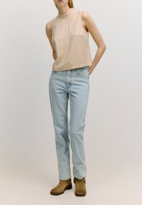 Beige ärmelloses Top mit hohem Ausschnitt, kombiniert mit hellblauen Jeans und braunen Stiefeletten, mit weichen Texturen und einem lässigen Schnitt.