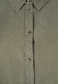 Olive green button-up shirt made of smooth fabric. Features a collar, seven buttons, and a vertical seam along the front.
