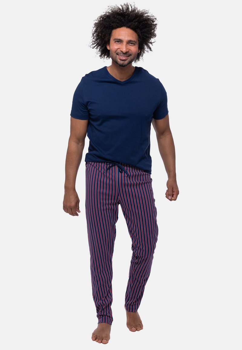 Marineblauwe t-shirt met korte mouwen gecombineerd met gestreepte loungebroeken met verticale rode en witte lijnen, van lichtgewicht stof en met een elastische tailleband.