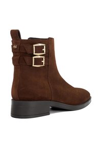 Brown suede ankle boot with a rounded toe, two gold buckle accents on the side, and a low black heel. Smooth texture with stitching details.