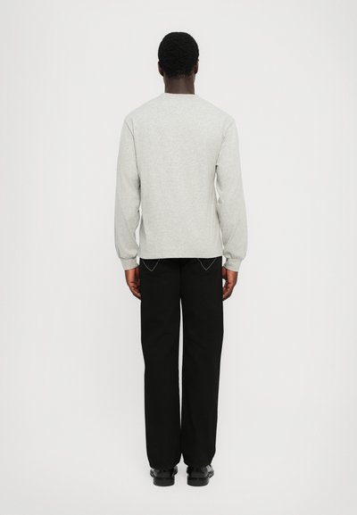 Gray long-sleeve sweatshirt with ribbed cuffs, paired with black tapered trousers and black shoes, viewed from the back.