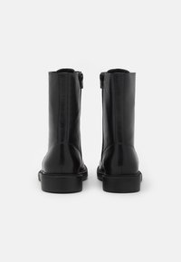 Bottes cheville noires en cuir lisse, dotées d'une fermeture éclair latérale et d'un bout arrondi. Semelles en caoutchouc noir robustes.