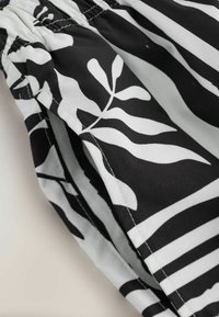 Tessuto in bianco e nero con motivi astratti di foglie e strisce, caratterizzato da cuciture visibili e una zona con elastico arricciato in vita.