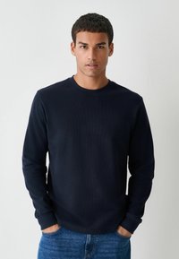 Diepblauwe langemouwen T-shirt in een gestructureerde stof, met een ronde halslijn en omgeslagen mouwen, gecombineerd met blauwe denim jeans.
