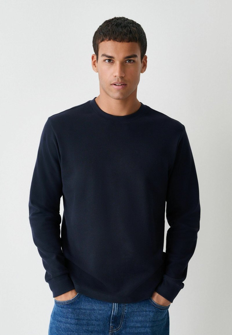 Diepblauwe langemouwen T-shirt in een gestructureerde stof, met een ronde halslijn en omgeslagen mouwen, gecombineerd met blauwe denim jeans.