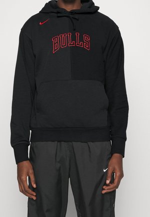 Person trägt schwarzen Kapuzenpullover mit rotem "BULLS"-Schriftzug und rotem Nike-Logo, kombiniert mit schwarzen Nike-Hosen.