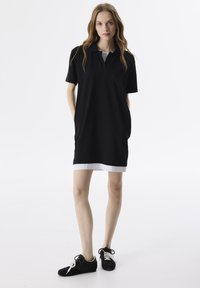 Czarna sukienka polo z krótkimi rękawami i białym brzegiem. Wykonana z gładkiego materiału, posiada kołnierzyk oraz boczne kieszenie. Połączona z czarnymi trampkami.