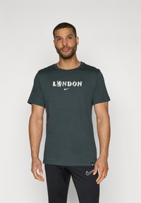 Tumši zaļš kokvilnas T-kreklis ar balto uzrakstu "LONDON" un lauvu grafiku centrā, kā arī Nike logo. Īsas piedurknes un apaļa kakla izgriezums.