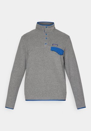 Grå fleece pullover med blå knaplukninger, krave med blåt kantbånd, brystlomme med klap og Patagonia-logo over lommen.