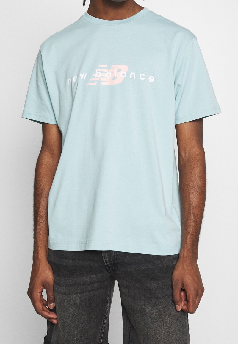 Světle modré bavlněné tričko s krátkými rukávy, s bílým a růžovým logem "New Balance" tištěným na hrudi. Klasický design s kulatým výstřihem.