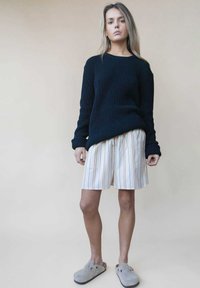 Marineblauwe ribbelgebreide trui, crèmekleurige gestreepte shorts met veelkleurige lijnen en grijze instappers. Ontspannen pasvorm met textuurlijke materialen.
