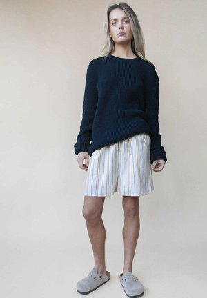 Pull en maille côtelée bleu marine, short crème à rayures multicolores, et chaussures gris à enfiler. Coupe décontractée avec des matériaux texturés.