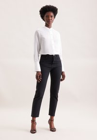 Camicia bianca a colletto con tessuto testurizzato, abbinata a jeans neri a vita alta e sandali neri con tacco.