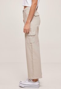 Beige cargo bukser laget av bomull, med sidelommer, en avslappet passform og rett ben-design, parret med hvite sneakers.