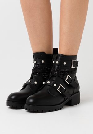 Bottines noires en cuir avec plusieurs sangles, boucles en argent et embellissements en perles. Talon chunky et accents texturés.