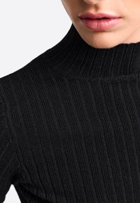 Schwarzer Rollkragenpullover mit gerippter Textur und figurbetontem Design, das subtile vertikale Linien und einen hohen Kragen aufweist.