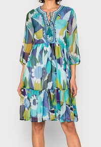 Šaty s květinovým vzorem vyrobené z lehkého materiálu. Mají tříčtvrteční rukávy, vrstvený design a výstřih ve tvaru klíčové dírky s detaily na třásních.