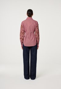 Gestreepte rood-witte shirt met geborduurde bruine mouwen, getailleerde pasvorm, met knoopmanchetten, gecombineerd met donkere wijde jeans.