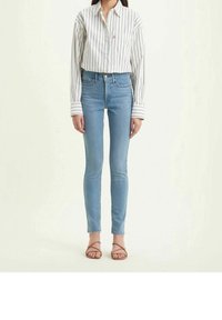 Jeans ajustados de color azul claro combinados con una camisa blanca y azul marino a rayas, con cierre de botones y mangas largas, complementados con sandalias marrones de tiras.