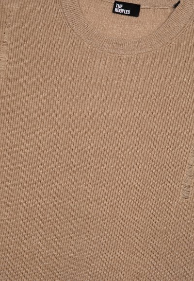 Beige Strickpullover mit geripptem Muster, rundem Ausschnitt und kleinen Used-Details an der Seite. Markenlabel am Kragen sichtbar.