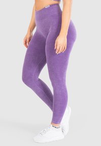 Leggings viola a vita alta con una finitura testurizzata e dettagli a coste verticali, abbinati a scarpe da ginnastica bianche.
