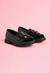 Mocasini din piele lacuita neagră, cu o curea texturată și un hardware distinctiv, având un toc masiv cu studuri decorative pe margine.
